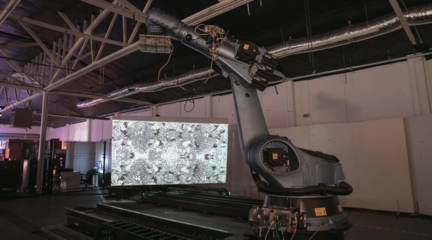 Image of large Kuka robots next to a projection screen