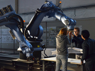 Three students grouped around a robot arm working on a physical model