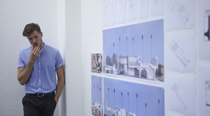 A male student standing presenting work on boards on the wall next to him