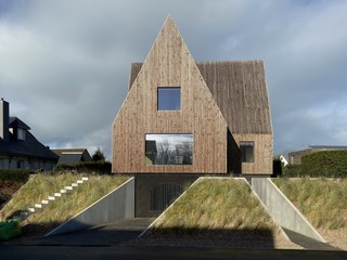 A photo of a wooden house in a triangular shape, with grass on the ground and clouds in the background
