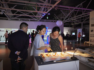 Two female students looking down at a model in a large warehouse space lit with purple lighting