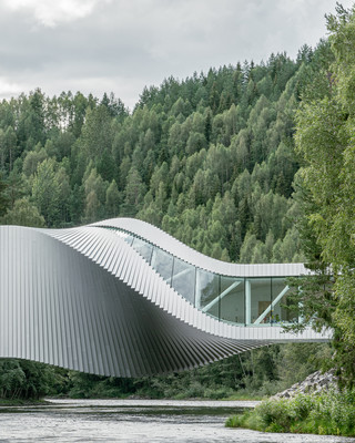 Image of a twisted building / bridge over a river in a forest.