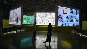two students standing in a gallery space with large screens displaying art work
