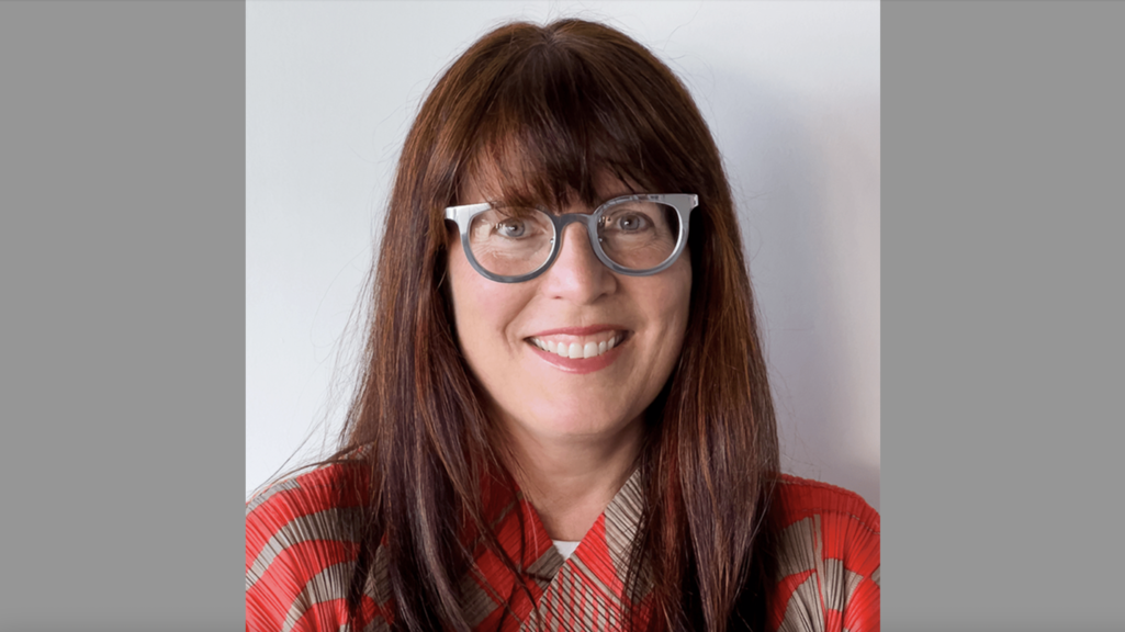 a photograph of a woman wearing glasses and a red shirt, smiling in front of a blank white background