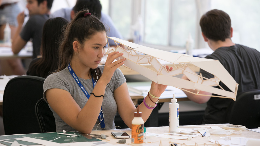 A female student sitting at a desk analyzing her model made of paper and wood