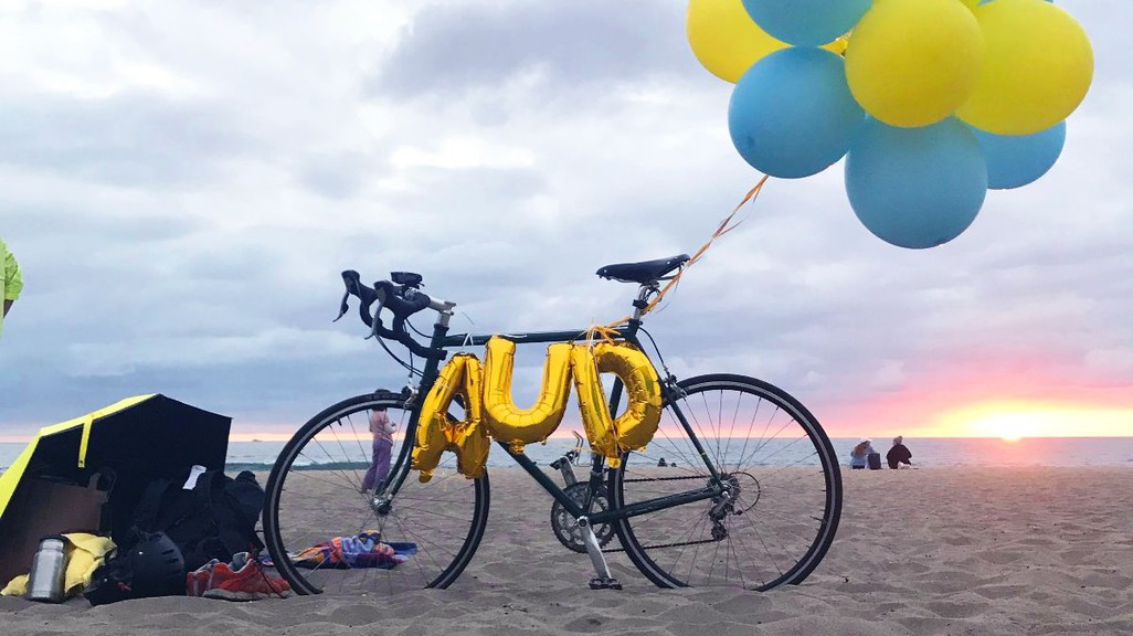 a photo of blue and yellow balloons tied to a bicycle on the beach